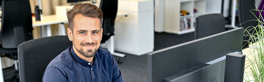 Markus, Product Manager SCD, sitzt am Laptop und lacht in die Kamera