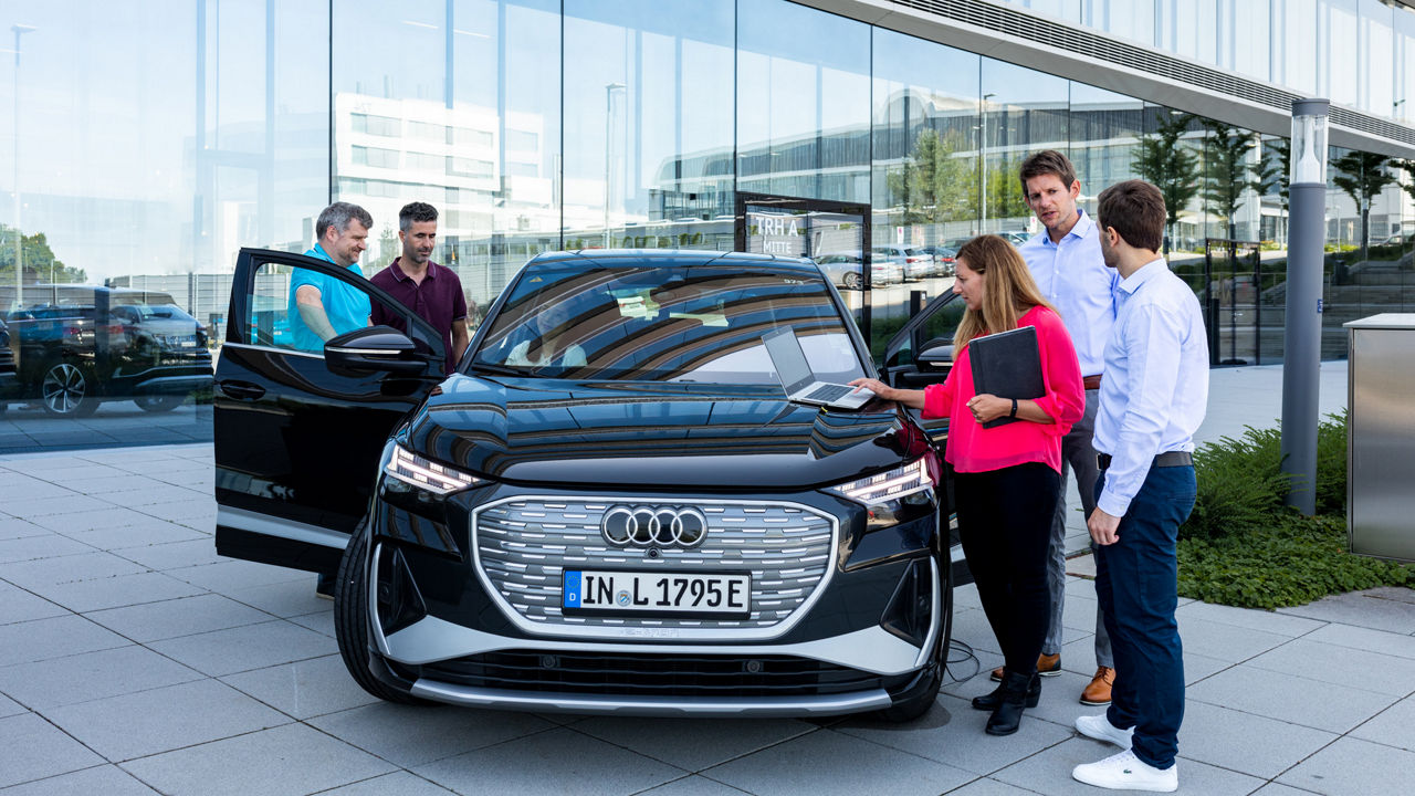 Five people are standing beside open Audi car doors, talking