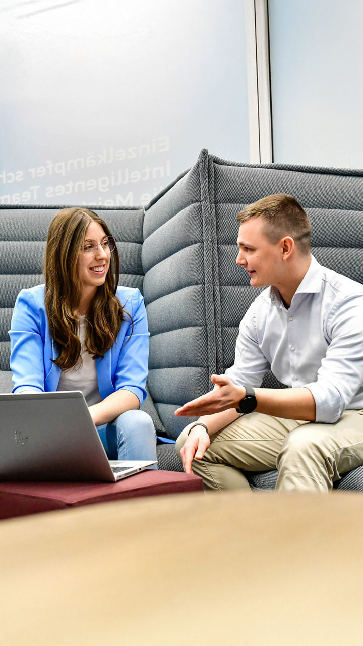 3 Student_innen haben ein Meeting in einer grauen Sitzecke im Büro