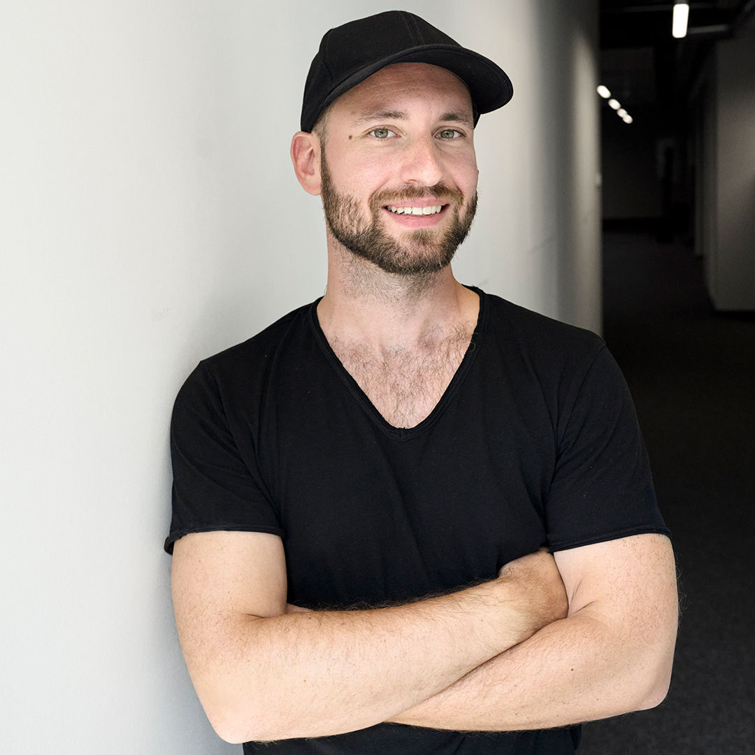 Sebastian Kister looks into the camera and wears a black shirt and cap.