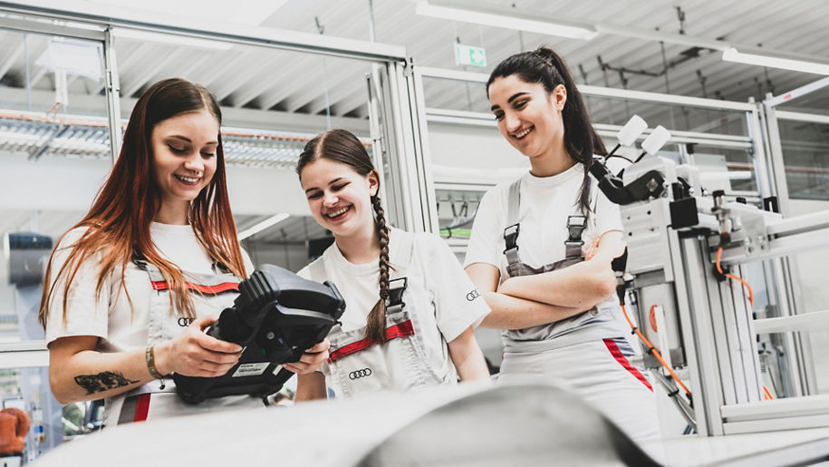 Drei Auszubildende stehen in der Produktion und schauen auf ein Elektrogerät