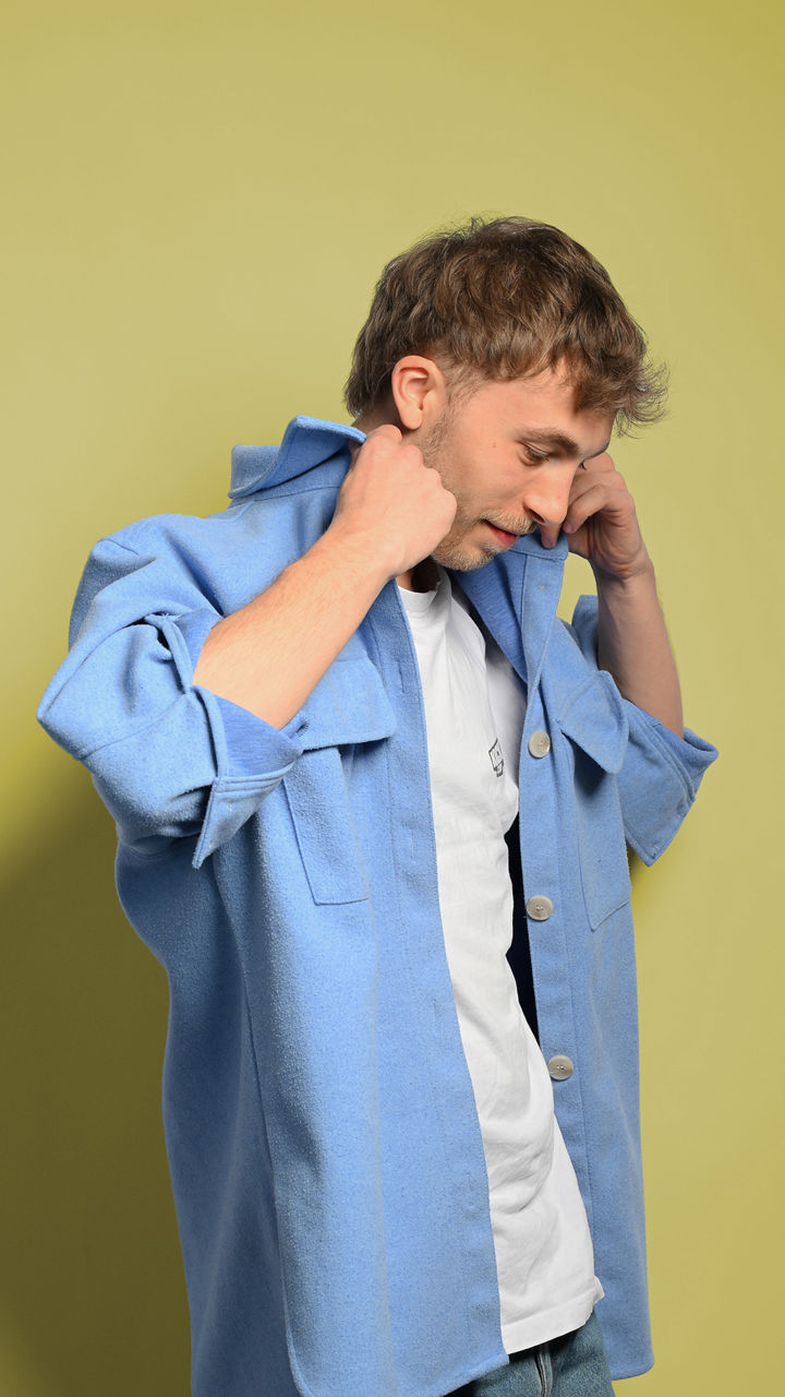 Julian schaut nach unten und richtet den Kragen seines blauen Hemdes 