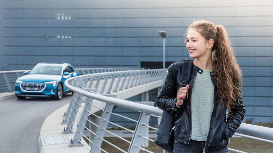 Mädchen mit Rucksack auf schaut nach links und hat einen blauen Audi hinter sich