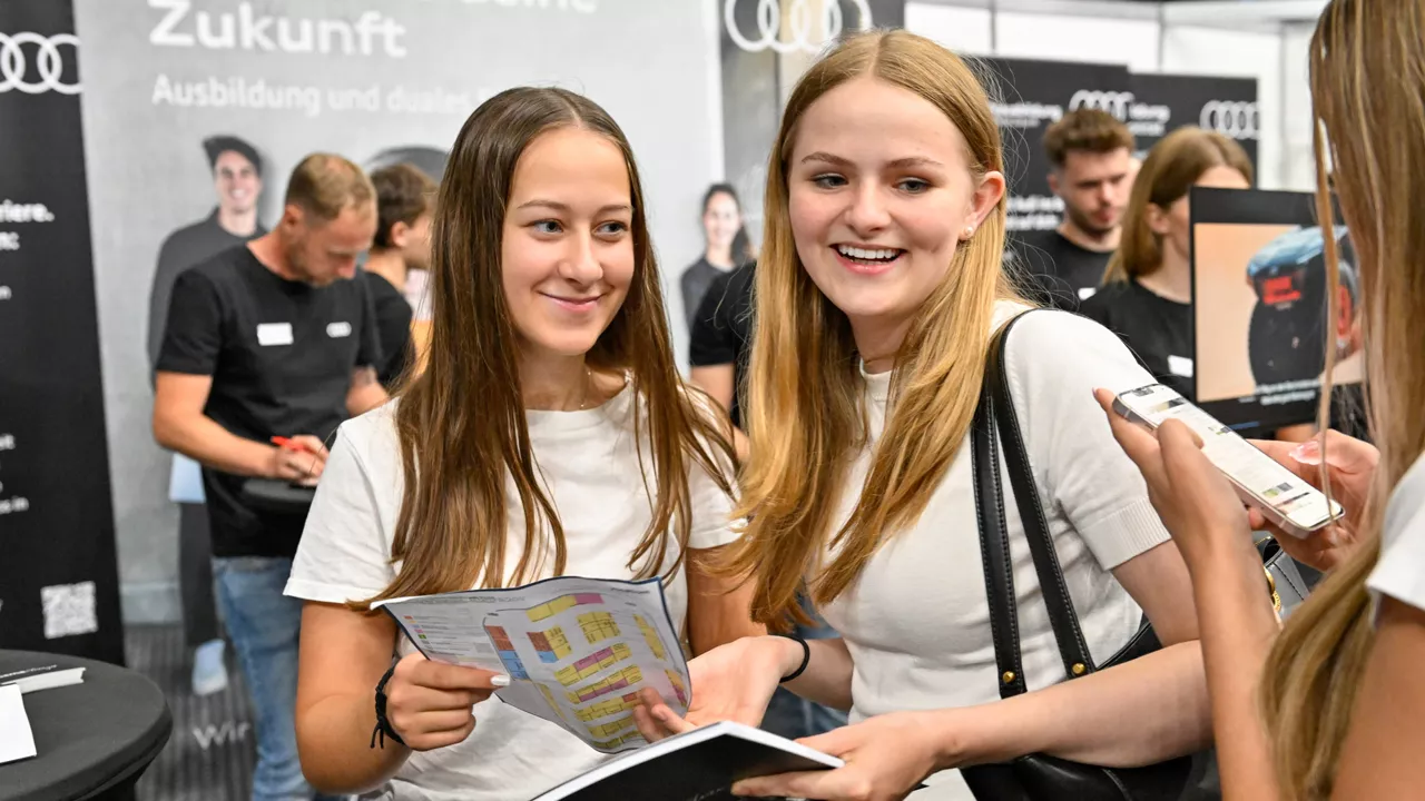 Zwei Personen sind auf einer Messe und unterhalten sich mit einer anderen Person mit Handy in der Hand
