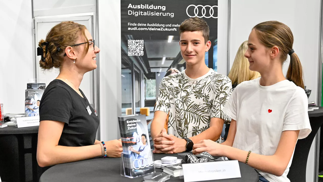 Drei Personen stehen um einen Stehtisch herum und ein Junge schaut dabei in die Kamera