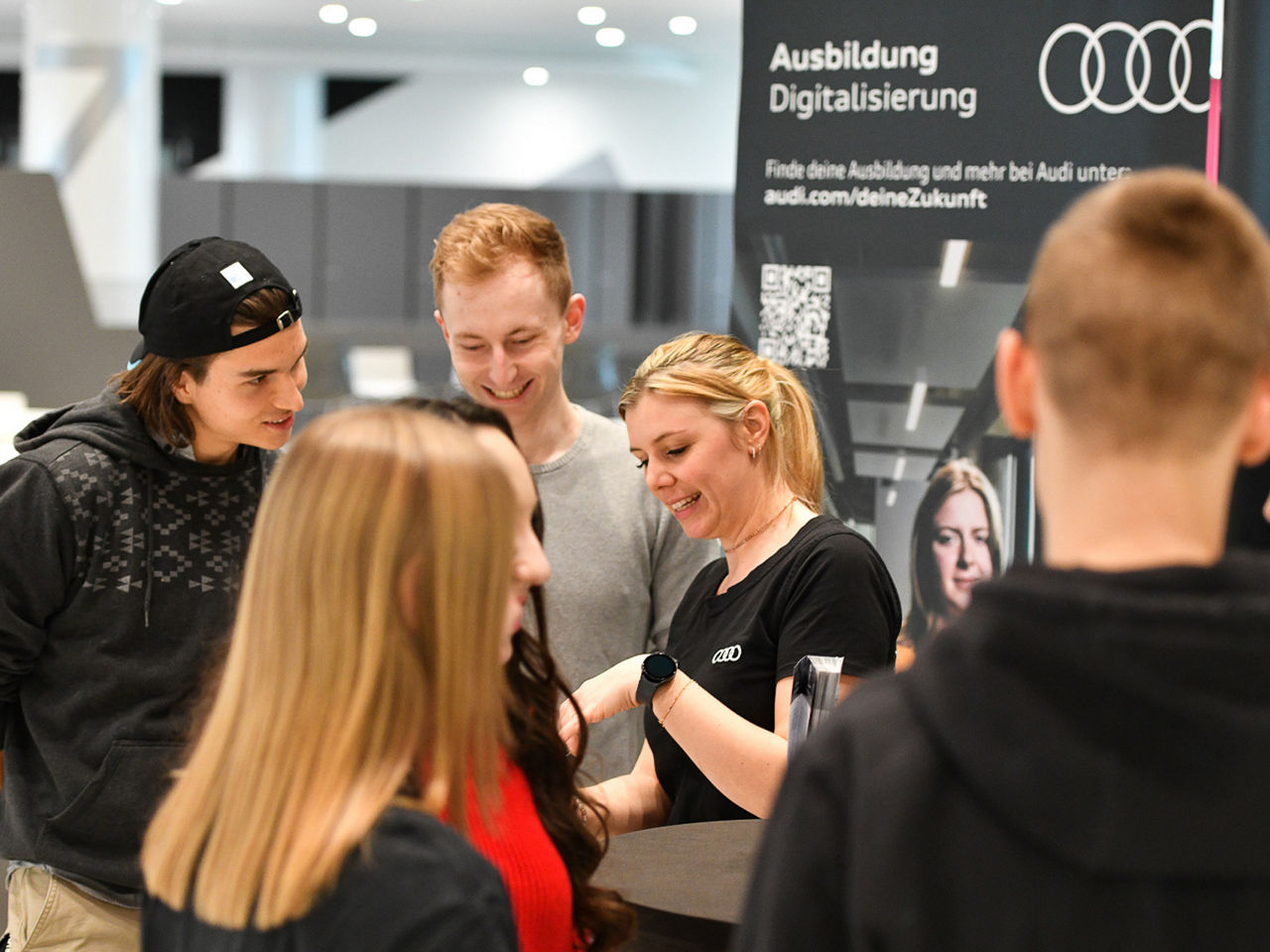 Eine Gruppe von jugendlichen Messegästen an einem Stand von Audi