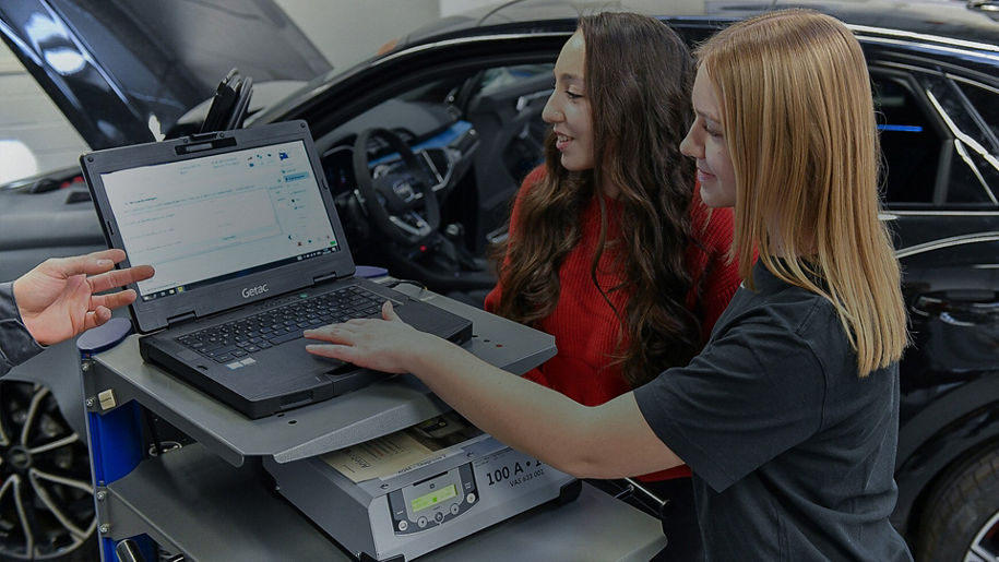Zwei Frauen stehen vor einem schwarzen Audi und schauen sich etwas auf einem Laptop an