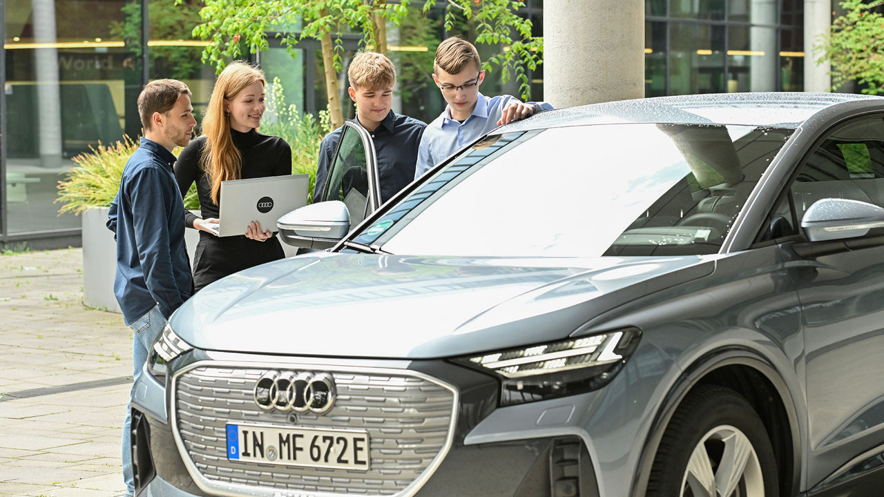 Four Audi employees are in conversation and stand behind an Audi
