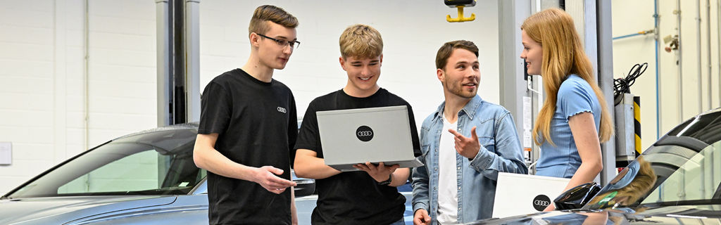 Four Audi employees are talking and looking at something on a laptop