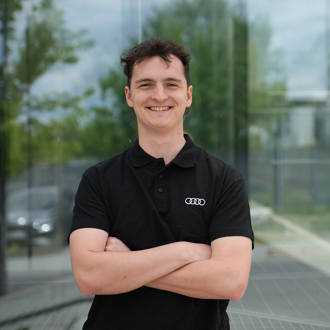 Ein Mann lacht in die Kamera mit verschränkten Armen und Audi-Shirt an