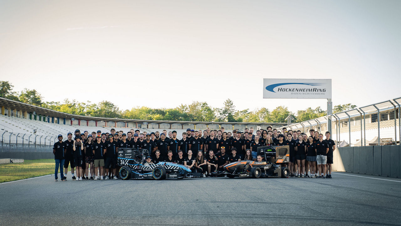 Gruppenfoto des Teams TUfast e.V. und Schanzer Racing e.V. mit ihren Fahrzeugen am Hockenheimring