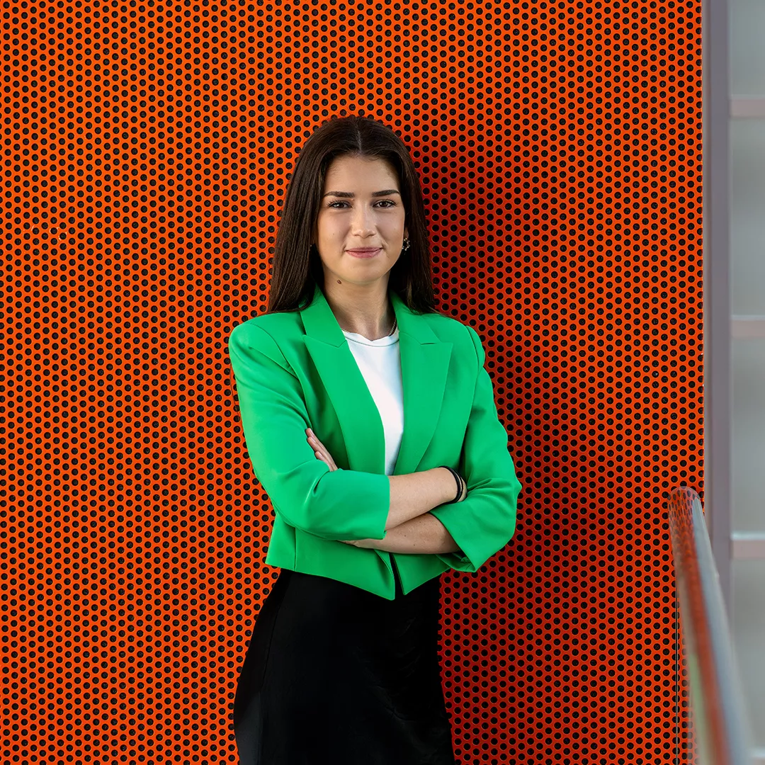 Alina stands with her arms crossed in front of a wall and smiles at the camera