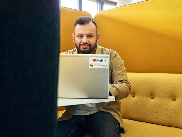 Buenyamin schaut in die Kamera und sitzt an einem Tisch mit einem Laptop vor sich