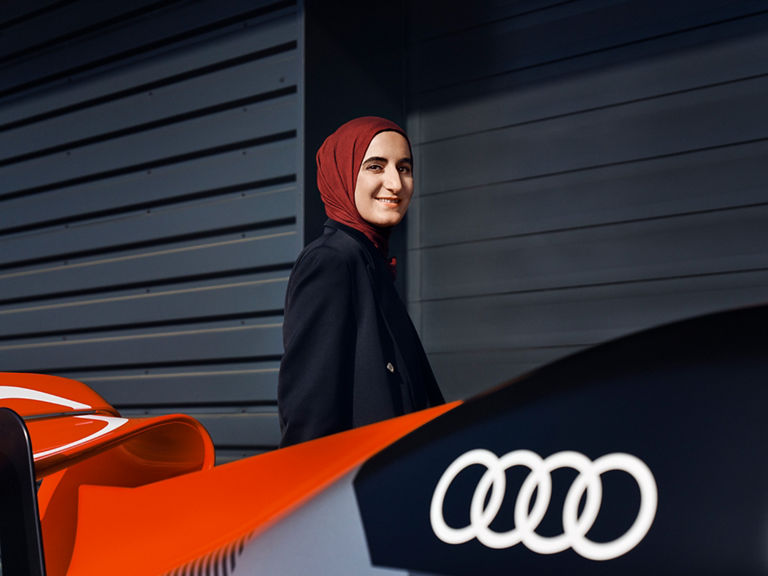 Sümeyye steht vor einem Formel 1 Wagen mit großem Audi Logo