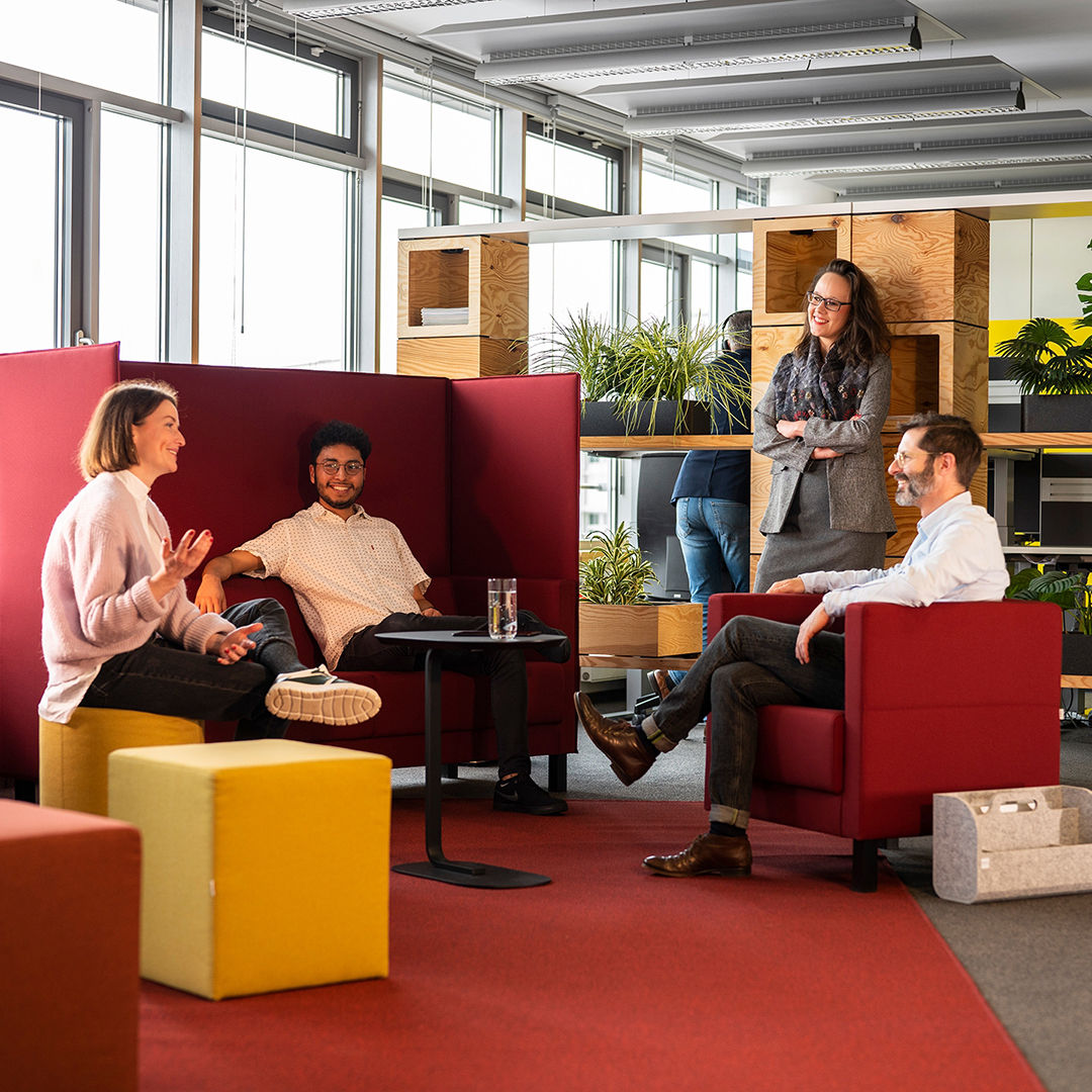 In a modern office, three people are talking while a fourth stands still