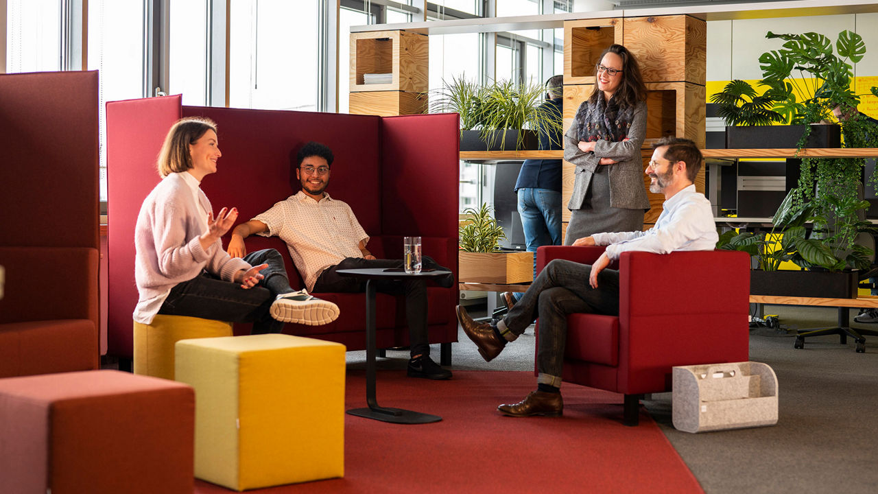 Mehrere Mitarbeitende sitzen im Kreis um einen Tisch herum und reden