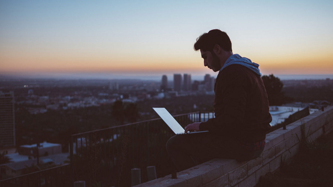 Man with laptop sitting on a wall