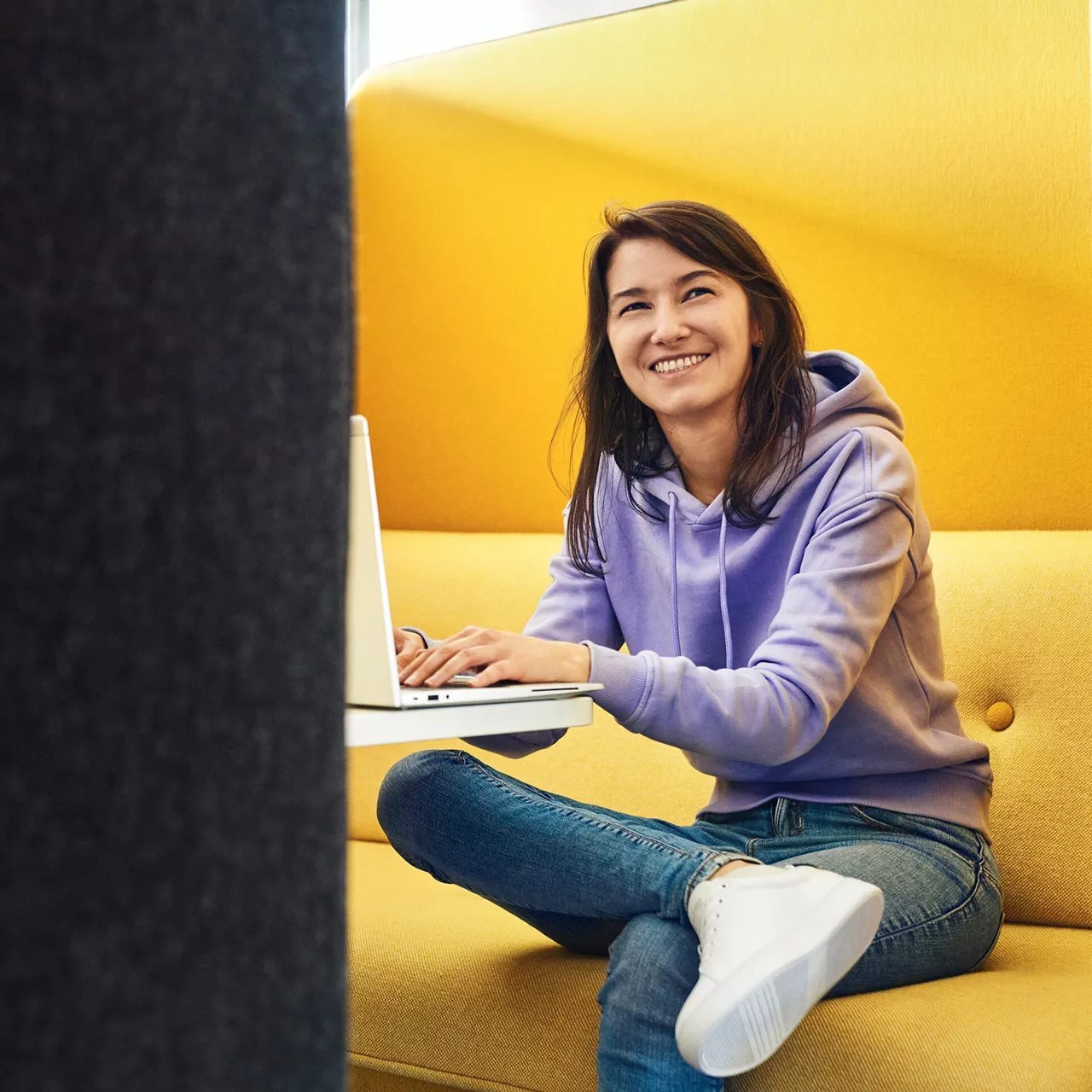Eine Frau lacht in die Kamera und tippt auf einem Laptop