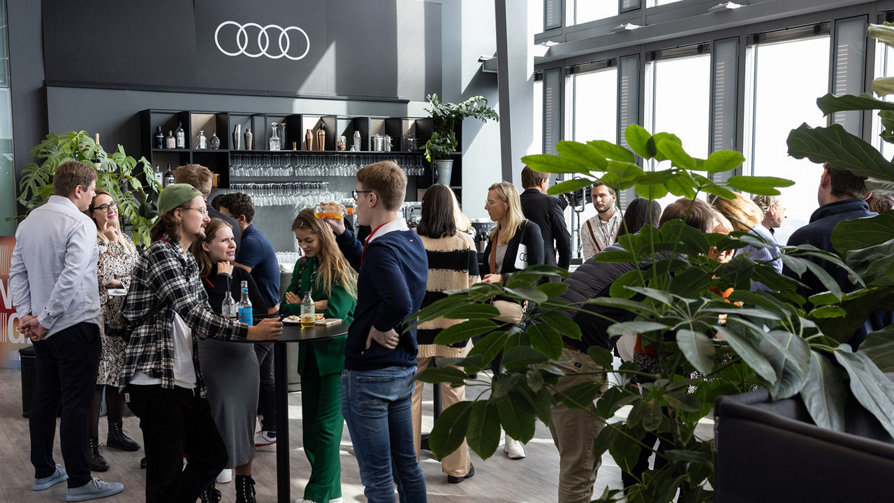 Mehrere Personen befinden sich in einem Raum mit Tischen und einer Bar und unterhalten sich