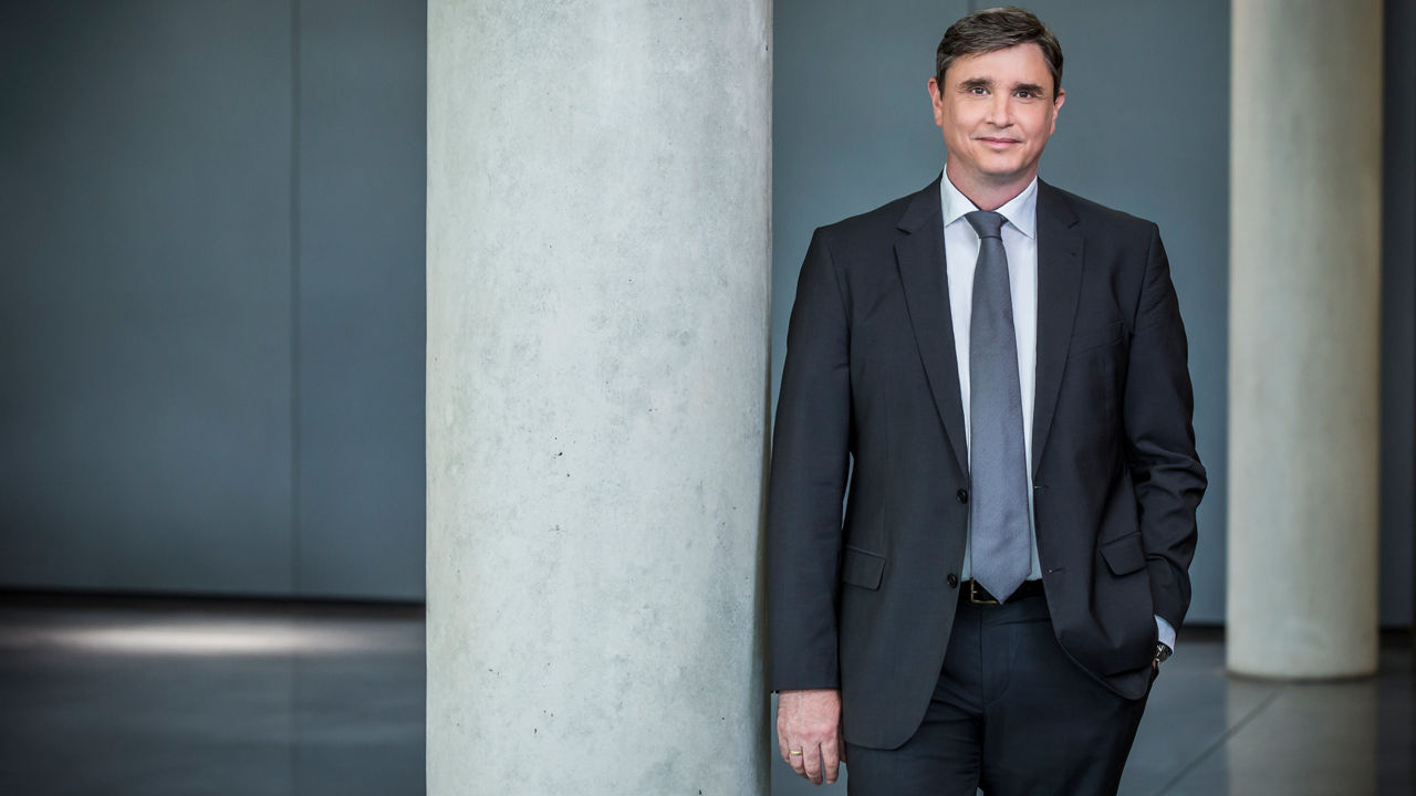 Jürgen Rittersberger, Member of the Board of Management of AUDI AG, Finance and Legal Affairs, leans against a grey pillar and looks into the camera