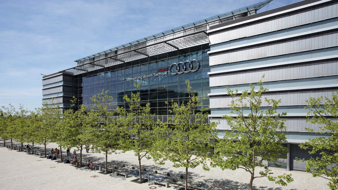 Image of a row of trees in front of the façade of the AUDI AG headquarters