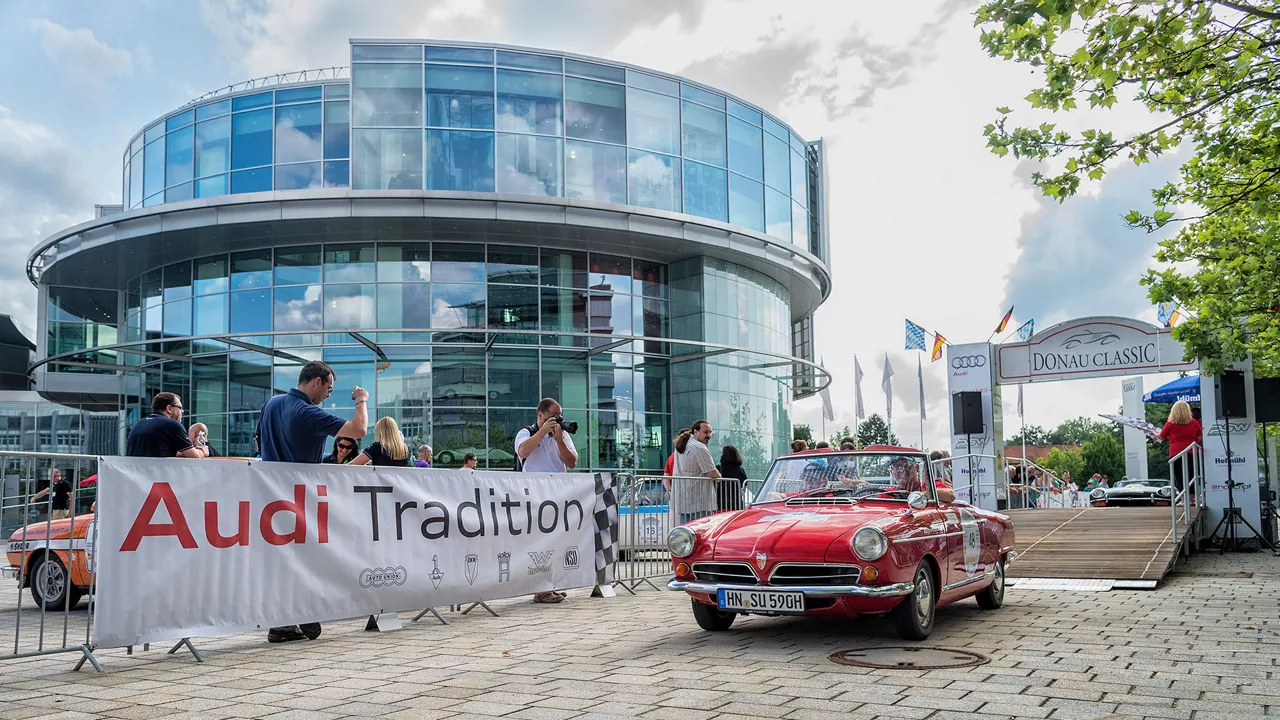 Ein rotes Audi Traditionsfahrzeug fährt an Zuschauern vorbei ei der Donau Classic