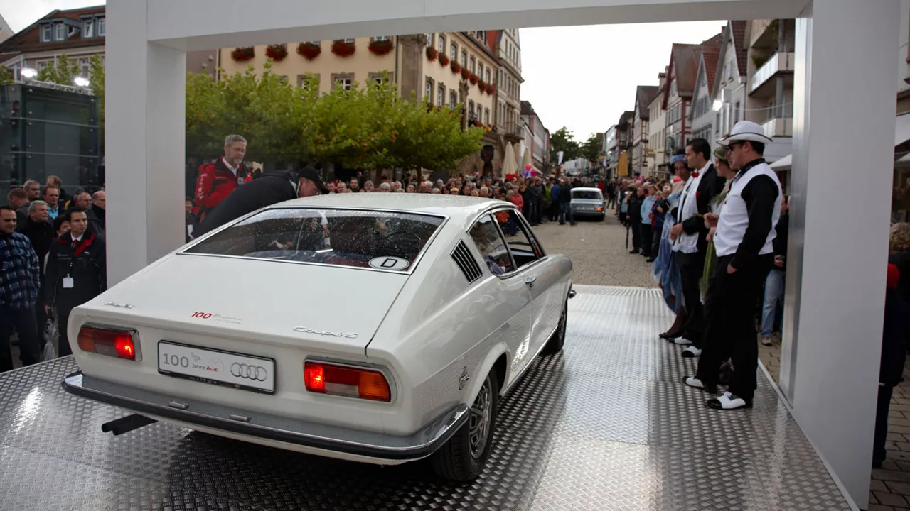 Heckansicht eines weißen Audi Traditionsmodells mit der Aufschrift "100 Jahre Audi"
