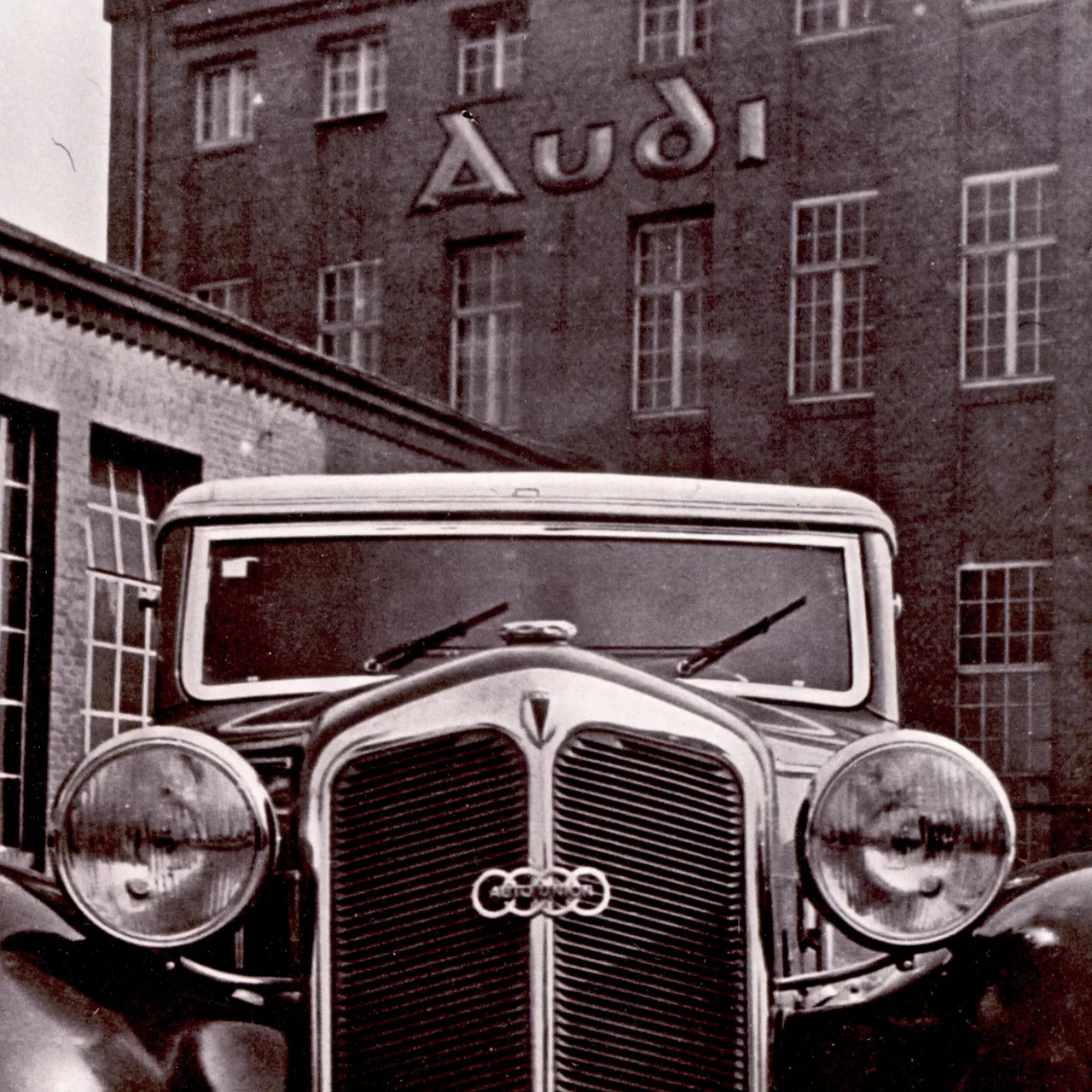 Close-up of a traditional Audi model in front of a historic Audi plant