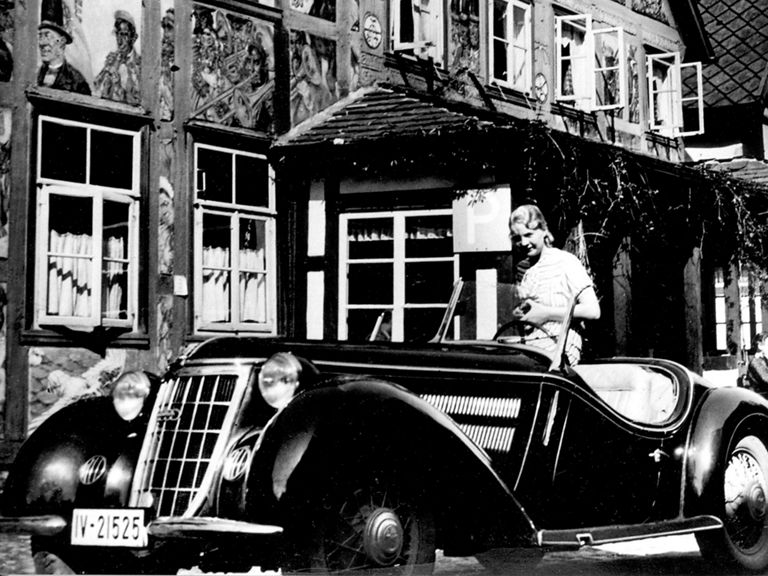 Schwarz-weiße Aufnahme von einer Frau, die auf einem Wanderer W 25 K vor einem Haus sitzt