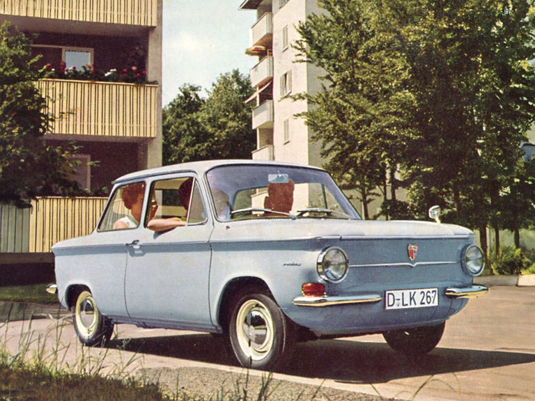 Farbige Aufnahme von mehreren Personen in einem hellblauen NSU Prinz vor Wohnhäusern 