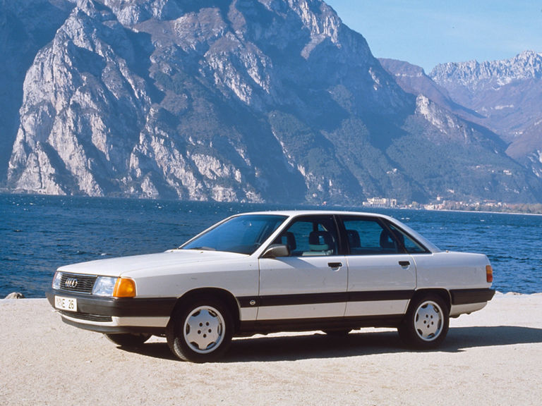 Ein weißer Audi 100 TDI in der Front-Seitenansicht von links vor einer Bergkulisse mit einem Bergsee