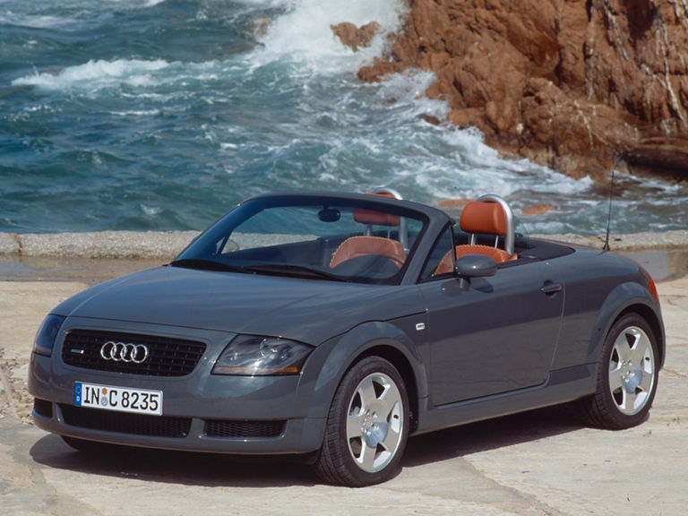 Ein grauer Audi TT Roadster quattro in der Front-Seitenansicht vor Felsen im Meer
