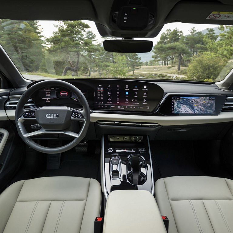 The interior view of an Audi with a modern, digital cockpit. The steering wheel and dashboard are accompanied by a large, seamless display that shows various vehicle information. The focus is on the digital controls and the elegant design of the vehicle interior.