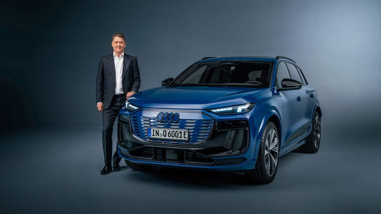 Gernot Döllner steht neben einem blau lackierten Audi Q6 e-tron