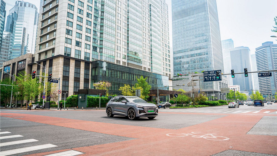 A silver Audi model stands in front of a backdrop of tower blocks