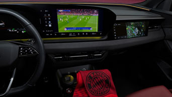 Recording of a dashboard with a football broadcast. An FC Bayern Munich scarf is on the gear stick