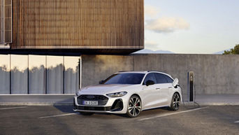 Audi A5 Avant e-hybrid quattro in glacier white stands at a charging station in front of a building with wooden panel cladding