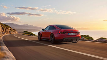 Roter Audi e-tron GT quattro fährt an der Küstenstraße bei Sonnenuntergang