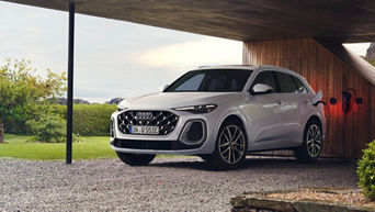 An Audi Q5 SUV e-tron in glacier white stands at a charging station in the countryside.