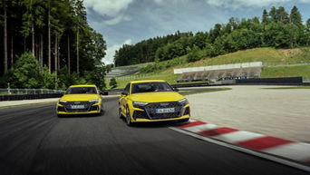 Zwei gelbe Audi RS3 fahren über eine Rennstrecke am Waldrand.
