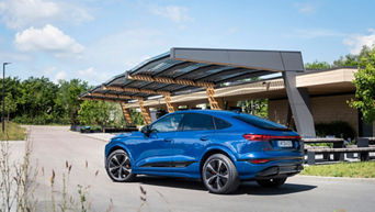 An Audi SQ6 Sportback e-tron in Ascari blue metallic is basking in the mid-day sun in front of a fast charging station.