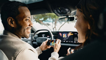A game from the AirConsole gaming platform runs on the touch display in an Audi. The driver and passenger smile at each other and each hold a smartphone in their hands. They use the smartphones as controllers to play the games.