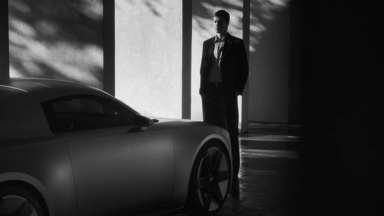 Harris Dickinson läuft seitlich am Audi Concept C vorbei. Das Auto ist von vorne zu sehen.