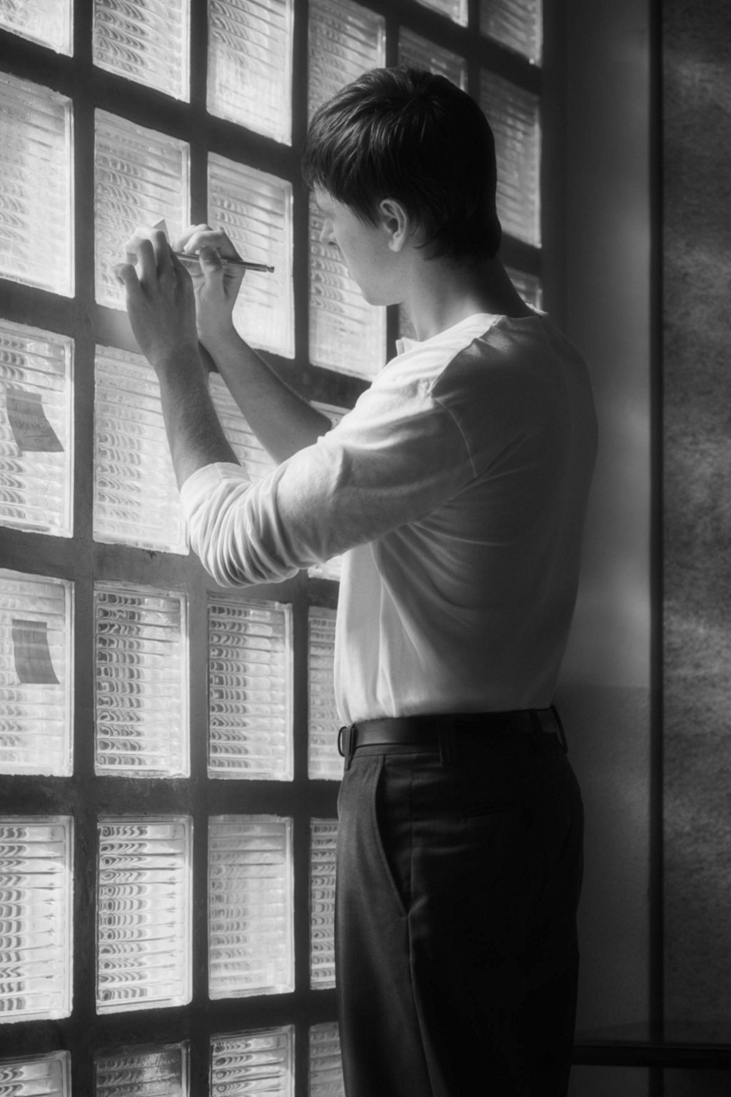 Harris Dickinson stands in front of a wall of glass blocks and takes notes.