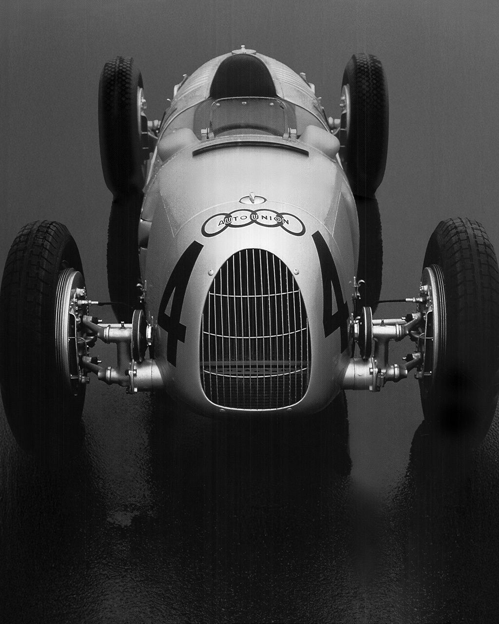 Front view of a historic Audi racing car with free-standing wheels against a grey background.
