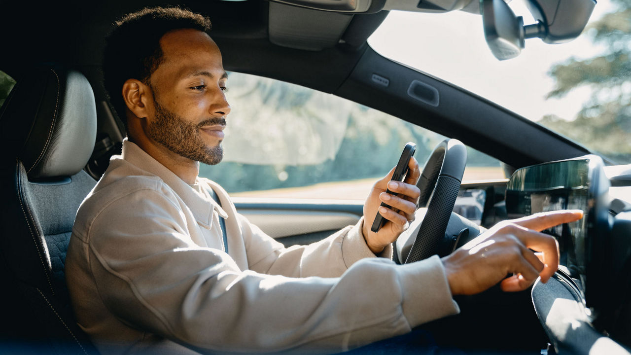 A man is sitting behind the wheel of his Audi. He is holding his smartphone in one hand while operating the vehicle's MMI with the other.