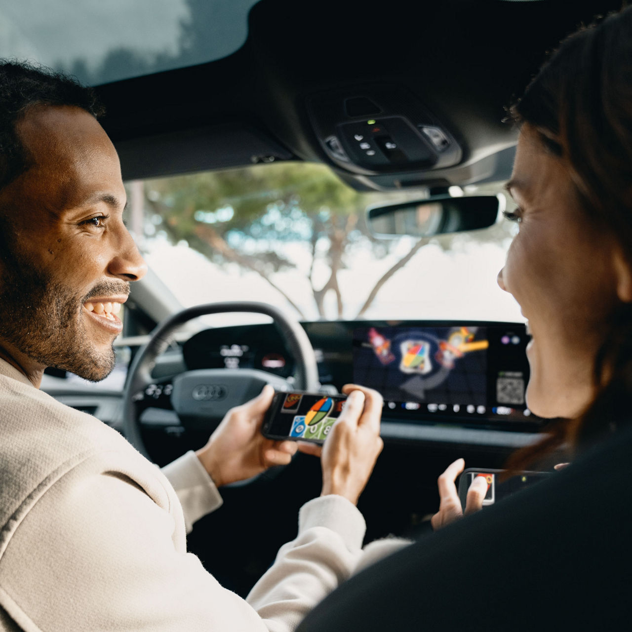 A couple is playing a game on the MMI of their Audi. They use their smartphones to control it.