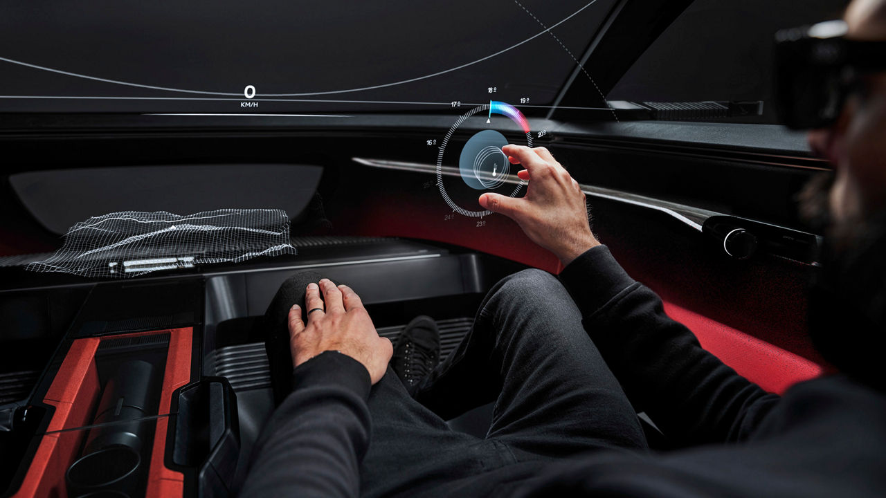 A futuristic vehicle cockpit without physical controls. A driver's hand reaches for a virtual button that floats freely in the air as a hologram.