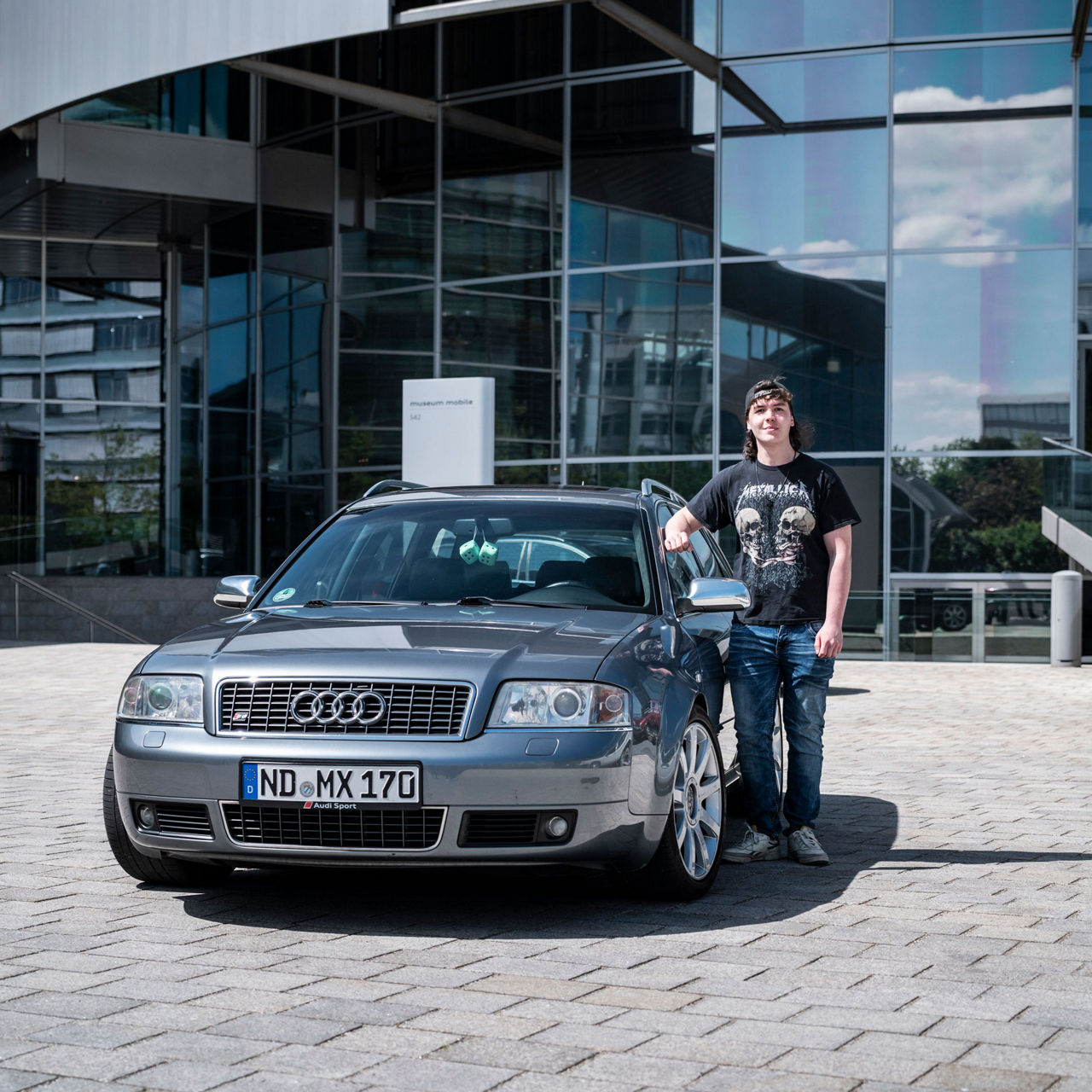 Maximilian Biber is standing next to his metallic-painted Audi S6 in a Metallica T-shirt and an upside-down baseball cap.