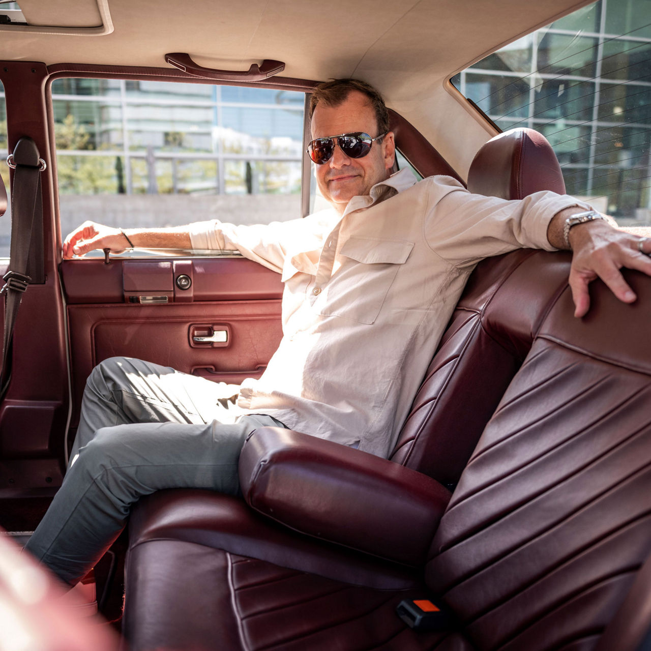 Gary Telaak sits relaxed on the red leather back seat of his Audi 5000 S wearing sunglasses and a light-colored linen shirt.